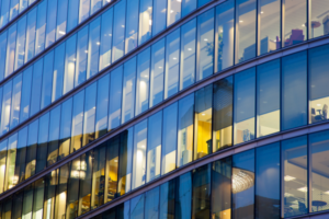 A glass office block with various offices lit up. It is night time.