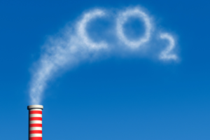 Smokestack emitting white smoke that forms the text “CO₂” against a blue sky, representing carbon emissions and environmental impact.