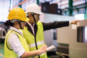 Two people in hard hats and hi vis. One holding a clipboard conducting an environmental audit